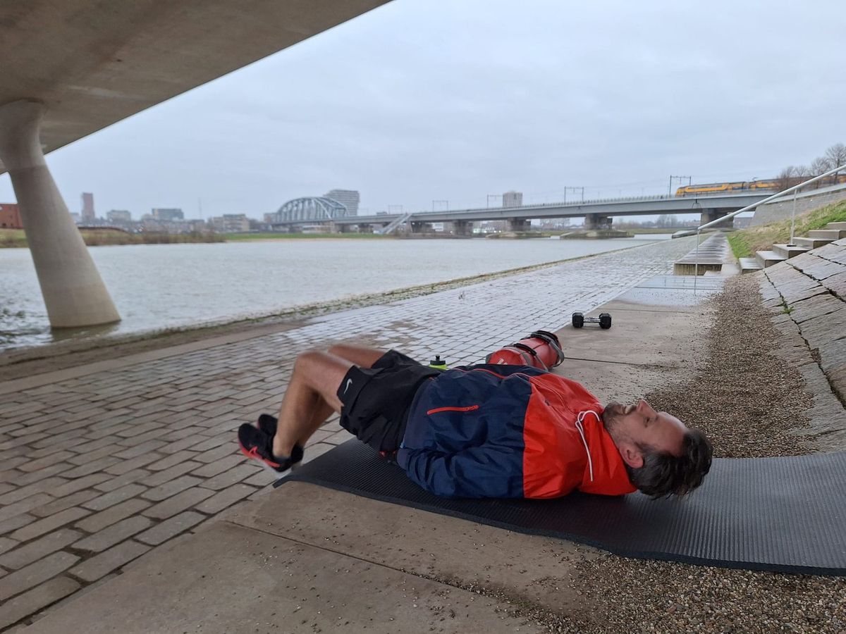Iemand traint met dumbells op een mat onder een brug